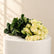 A bouquet of pale yellow roses with dark green leaves, arranged on a white sheet over a beige storage cabinet against a white marble-patterned background.