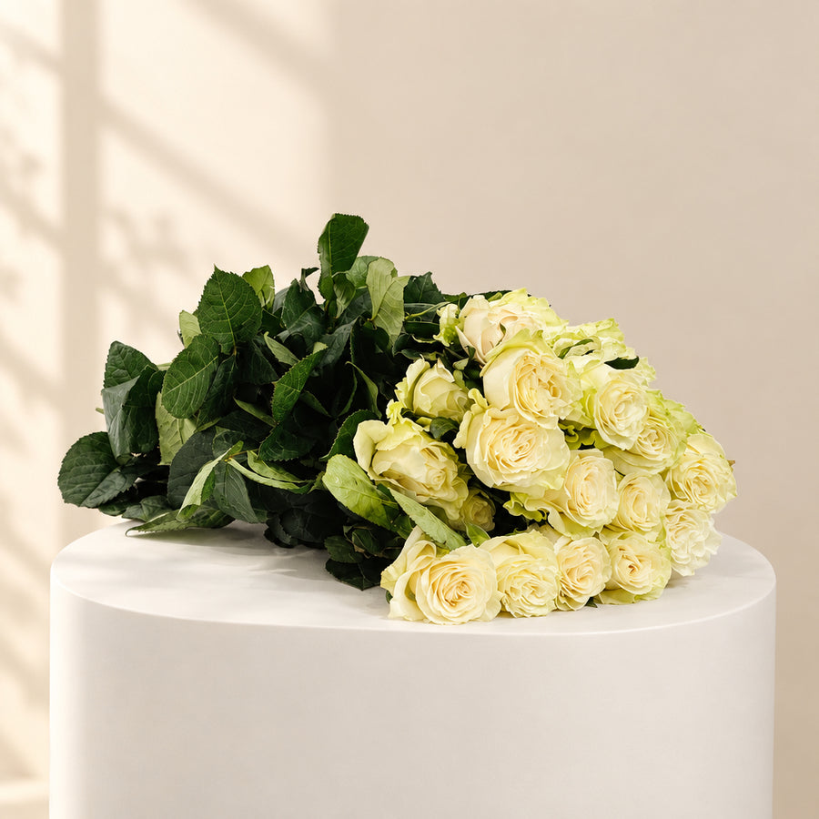 A bouquet of pale yellow roses with dark green leaves, arranged on a white sheet over a beige storage cabinet against a white marble-patterned background.