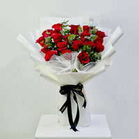 A bouquet of red roses wrapped in white paper with a black ribbon, displayed on a white pedestal against a light gray background.