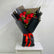 A bouquet of red roses wrapped in black paper with a bright red ribbon, displayed on a white pedestal against a light gray wall.