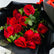 A bouquet of red roses wrapped in black paper with a small gold floral label, photographed close up against a light neutral background.
