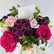 A vibrant floral bouquet featuring bright pink and magenta roses, light pink carnations, deep purple chrysanthemums, and green eucalyptus leaves, arranged in a white vase with a 'VIVA FLORA' card.