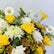 A vibrant floral arrangement featuring bright yellow roses, white daisies, white roses, and white chrysanthemums, accented by green eucalyptus leaves and small brown chrysanthemums, with a small white card in the center.