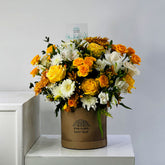 A vibrant floral arrangement in a round brown cardboard box with the brand name 'VIVA FLORA' printed on it, set on a white marble surface against a light gray wall.