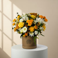 A vibrant floral arrangement in a round brown cardboard box with the brand name 'VIVA FLORA' printed on it, set on a white marble surface against a light gray wall.