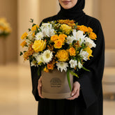 A vibrant floral arrangement in a round brown cardboard box with the brand name 'VIVA FLORA' printed on it, set on a white marble surface against a light gray wall.