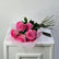 A bouquet of pink roses wrapped in pale pink tissue paper and a black ribbon, displayed on top of a white cabinet against a light gray wall.