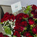 A bouquet of deep red roses with green leaves and small white baby's breath flowers, arranged in a gift box with a card that reads 'VIVA FLORA Arabic Love'.
