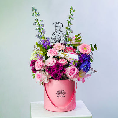 graduation Pink bucket filled with colorful flowers on a white surface with a light gray background