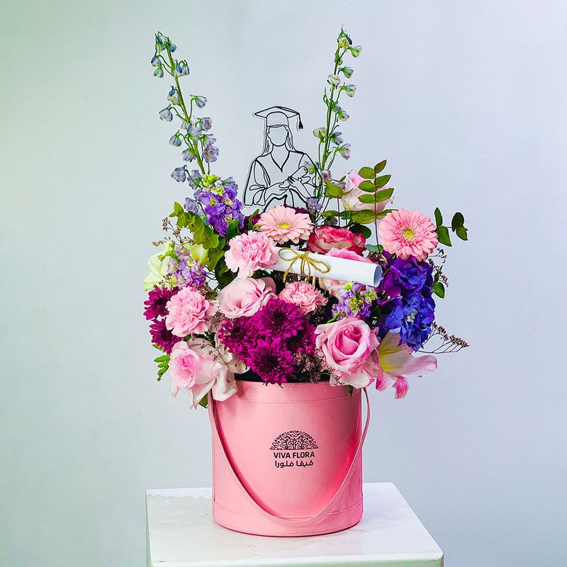 graduation Pink bucket filled with colorful flowers on a white surface with a light gray background