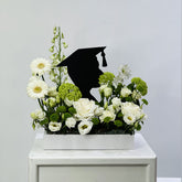 Floral arrangement with a black graduation cap silhouette on a white surface against a light gray background