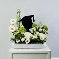 Floral arrangement with a black graduation cap silhouette on a white surface against a light gray background