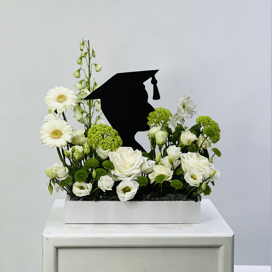 Floral arrangement with a black graduation cap silhouette on a white surface against a light gray background