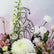 A graduation-themed floral arrangement with white and pink flowers surrounding a black line-art silhouette of a graduate holding a diploma, set against a soft pink and white background.