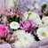 A close-up of a floral bouquet with pink and white flowers, including roses, chrysanthemums, daisies, and alstroemeria, wrapped in pale pink paper.