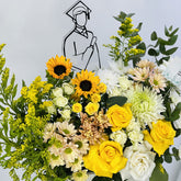 A vibrant graduation flower bouquet featuring yellow sunflowers, yellow and white roses, white and pale yellow daisies, green eucalyptus, and yellow bird's eye flowers, arranged in front of a white background with a simple black line drawing of a graduate.