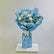 A bouquet of blue and white flowers wrapped in light blue paper and tied with a white ribbon, displayed on a white pedestal against a light gray background.