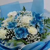 A floral bouquet featuring blue and white flowers, including carnations, roses, and baby's breath, wrapped in light blue tissue paper.