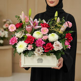 A vibrant floral arrangement in a cream-colored rectangular box on a white pedestal, featuring pink, red, white, and green flowers with a gold 'Happy Birthday' sign, from the brand VIVA FLORA.