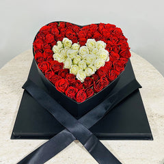 Heart-shaped box filled with red and white roses on a light surface.