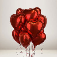 A cluster of shiny red heart-shaped foil balloons tied together with thin strings, photographed against a plain light gray studio background.