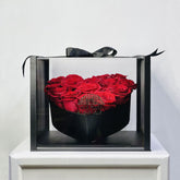 Heart-shaped box of red roses with a black ribbon on a white pedestal against a light gray background
