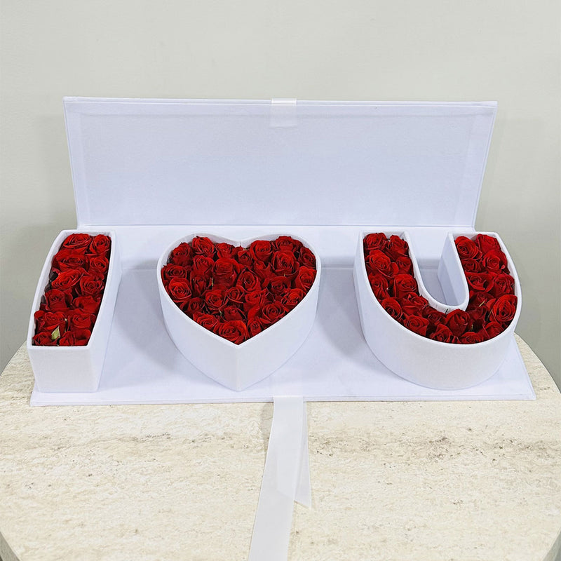 Three white letter-shaped boxes filled with red Baby roses on a light surface. best budget friendly Arrangement for the valentines day love proposal 