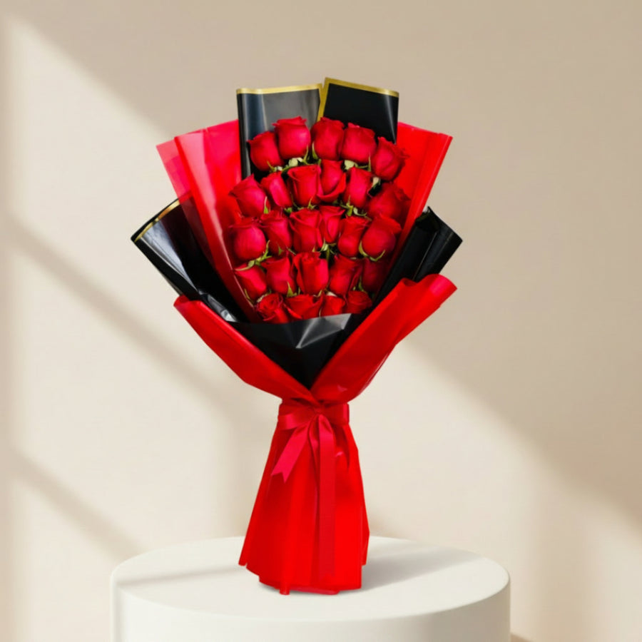 A bouquet of 24 red roses wrapped in bright red and black paper with a red ribbon printed with 'Viva Flora',