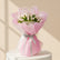 A bouquet of white tulips wrapped in pink tissue paper and tied with a silver ribbon, held by a person whose arm is visible on the left side, set against a marble-patterned wall background.