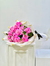 A bouquet of pink roses wrapped in white paper with gold trim and a black ribbon, displayed on a white pedestal against a plain light background.