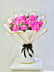 A bouquet of pink roses wrapped in white paper with gold trim and tied with a black ribbon, displayed on a white pedestal against a light gray background.