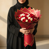 A large bouquet of red and white roses wrapped in red paper with gold edges, displayed on a white pedestal against a plain light background.