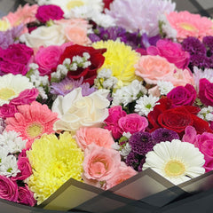 Colorful mixed flower bouquet with roses and chrysanthemums in black wrapping