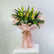 A fresh flower bouquet wrapped in light pink tissue paper and tied with a rustic jute twine bow, displayed on a white pedestal against a neutral light gray background.