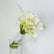A bouquet of white calla lilies with green stems wrapped in white lace, displayed in a clear glass vase against a light gray background.