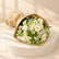 A bouquet of white and light yellow flowers with green foliage, wrapped in brown kraft paper, resting on a white cabinet against a white marble-patterned wall.