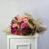 A close-up of a wrapped bouquet of roses and chrysanthemums in soft pink, peach, magenta, and muted tan tones, with pale brown tissue paper wrapping visible on the right side.