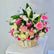 A vibrant floral arrangement in a woven wicker basket, featuring pink and white flowers, green leaves, and a small card, displayed on a white surface against a light gray background.
