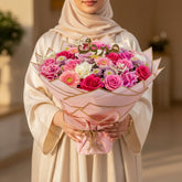 Bouquet of flowers wrapped in pink paper with gold accents on a white surface.