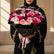 A large floral bouquet with pink, red, and white roses and purple chrysanthemums, wrapped in black paper with gold trim and a pink ribbon, displayed on a white pedestal against a light gray wall.