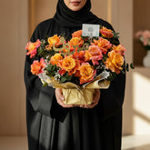 Bouquet of orange and pink roses with a decorative card on a white surface.