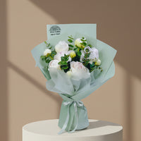 A bouquet of Peony with green eucalyptus stems, wrapped in pale mint green tissue paper and tied with a matching ribbon. A card at the top reads VIVA FLORA