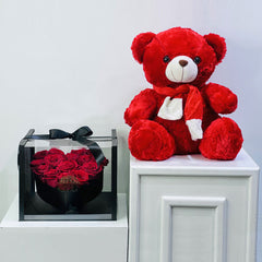 Red teddy bear and box of red roses on a white surface with a light gray background, perfect combo on this valentines day 