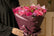 Qatari lady holding A vibrant bouquet of pink roses and purple flowers wrapped in dark purple paper, tied with a jute twine bow, 