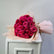 A bouquet of deep pink roses wrapped in pale blush paper, placed on top of a white cabinet against a light gray wall.
