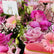 A close-up of a pink floral bouquet with roses, gerbera daisies, baby's breath, and green filler stems, with a small card reading VIVA FLORA and a gold ring holder.