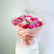 A vibrant bouquet of pink, magenta, and white roses with gerbera daisies, wrapped in pink paper with gold geometric borders and tied with a pink ribbon, displayed on a white pedestal against a light gray background.