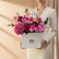 A vibrant pink floral arrangement featuring roses, hydrangeas, and daisies in a white square box with the brand name 'VIVA FLORA' printed on the front, displayed on a white pedestal against a white wall.