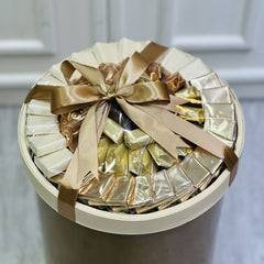 Round gift box filled with gold-wrapped chocolates on a neutral background