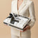 A boxed assortment of white and dark chocolates tied with a black ribbon printed with the brand name VIVA FLORA, displayed on a beige pedestal against a warm beige background.
